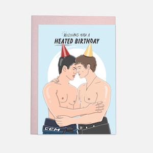 Op de afbeelding: Verjaardagskaart met een illustratie van twee mannen zonder shirt die elkaar omhelzen en feesthoeden dragen. De kaart heeft de tekst "Wishing you a Heated Birthday" op een lichtblauwe achtergrond. De kaart zit in een roze envelop.