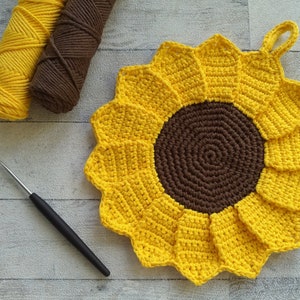 Può includere: Un sottopentola all'uncinetto a forma di girasole con un centro marrone e petali gialli. Il sottopentola ha un anello per appenderlo.