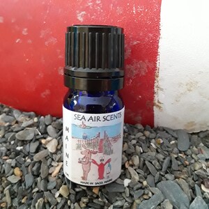 May include: A small blue glass bottle with a black cap. The bottle has a label that says "Sea Air Scents Maine" and features a cartoon moose and lobster. The label also says "Made in Saco, Maine".