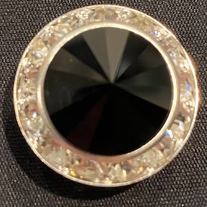 May include: A black onyx cabochon set in a silver ring with a clear crystal halo.