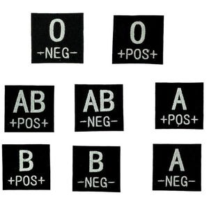 Può includere: Otto toppe quadrate nere con testo bianco ricamato, che mostrano i gruppi sanguigni: O, AB, A e B, con designazioni positive e negative. Le toppe sono disposte a griglia.