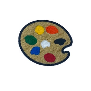 Op de afbeelding: Een bruin en zwart kunstenaars palet met zeven verfputjes. De putjes zijn gevuld met rode, oranje, gele, groene, blauwe, witte en zwarte verf.