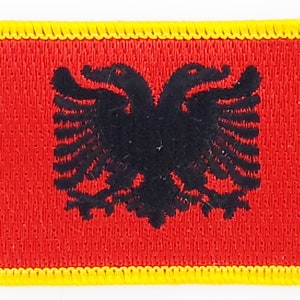 Könnte beinhalten: Ein roter Stoff-Patch mit einem schwarzen Doppelkopfadler in der Mitte. Der Patch hat einen gelben Rand.