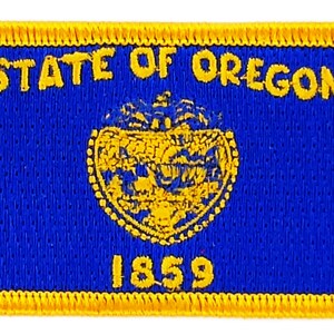 May include: A blue and gold embroidered patch with the text "STATE OF OREGON" and the year "1859" in the center. The patch features a stylized image of the state seal of Oregon.