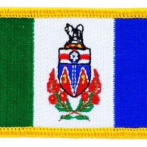 Könnte beinhalten: Gestickter Aufnäher mit der Flagge von Yukon, Kanada. Der rechteckige Aufnäher hat einen grünen vertikalen Streifen auf der linken Seite, einen blauen vertikalen Streifen auf der rechten Seite und eine weiße Mitte mit dem Yukon-Wappen.