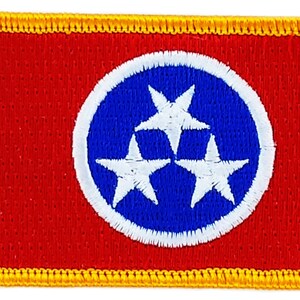 May include: A red and blue embroidered patch with a white circle containing three white stars. The patch is surrounded by a yellow border.