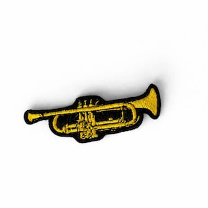 Könnte beinhalten: Ein gold-schwarzer, gestickter Aufnäher in Form einer Trompete. Der Aufnäher zeigt ein detailliertes Design des Instruments, mit Glocke und Rohren deutlich sichtbar. Er ist wahrscheinlich für Kleidung oder Accessoires bestimmt.
