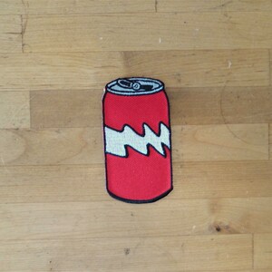 Könnte beinhalten: Roter und weißer gestickter Bügelaufkleber mit einer Dose Limonade.