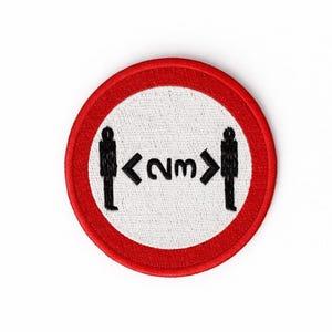 Peut inclure: Écusson rond brodé avec une bordure rouge et un centre blanc. Le motif présente deux silhouettes noires de personnes avec une flèche et le texte "2m" entre elles, indiquant une consigne de distanciation sociale.