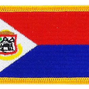 Op de afbeelding: Geborduurde patch met de vlag van Sint Maarten. Het vlagontwerp omvat een witte driehoek, rode en blauwe horizontale strepen en een wapenschild. De patch heeft een gele rand.