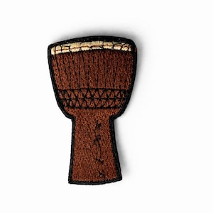 May include: Embroidered patch of a brown djembe drum with a black outline. The drumhead is tan, and the body is a darker brown. The patch is a musical instrument accessory.