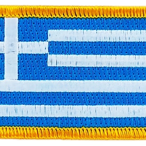 May include: A blue and white Greek flag patch with a yellow border. The flag is made of fabric and has a stitched edge.