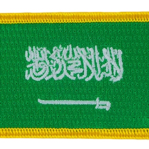 Puede incluir: Un parche verde bordado con una inscripción árabe blanca y una espada blanca, rodeado de un borde amarillo.