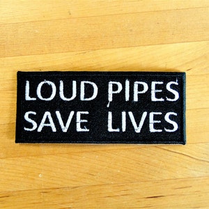 Puede incluir: Parche negro con texto blanco que dice "Loud Pipes Save Lives".