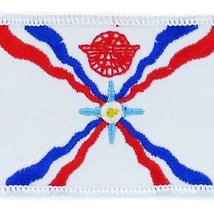 Puede incluir: Parche blanco bordado con un diseño rojo, blanco y azul. El diseño presenta una estrella con un círculo en el centro y un círculo rojo con un diseño de pájaro estilizado arriba.