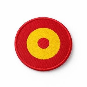 Può includere: Toppa ricamata circolare rossa con un cerchio interno giallo e un punto centrale giallo. La toppa ha un bordo cucito. È progettata per essere cucita o stirata sul tessuto. Il design è semplice e audace.