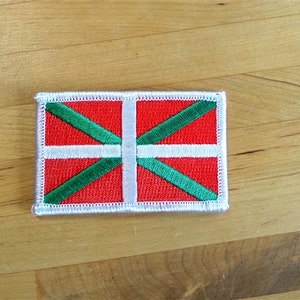 Peut inclure: Un écusson blanc avec un fond rouge et une croix verte. La croix est formée de deux lignes diagonales qui se croisent au centre de l'écusson.