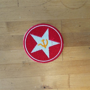 May include: A red embroidered patch with a white five-pointed star and a yellow hammer and sickle inside the star.