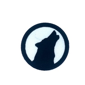 Può includere: Una toppa ricamata in bianco e nero di un lupo che ulula alla luna. Il lupo è in silhouette su un cerchio bianco con un contorno nero.