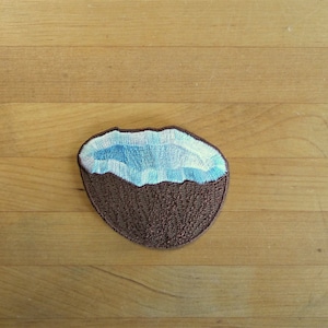 Puede incluir: Un parche de coco marrón con un interior bordado en azul y blanco.