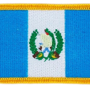 May include: A blue, white and green embroidered patch featuring the national flag of Guatemala. The flag depicts a quetzal bird with a green crest and a white breast, surrounded by green leaves.
