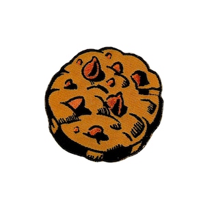 Puede incluir: Parche bordado con una galleta de dibujos animados con chispas de chocolate. La galleta es de color marrón claro con detalles en marrón oscuro y naranja. El parche tiene un borde negro sobre un fondo blanco.