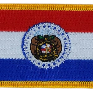 以下が含まれることがあります： 金色の縁取りのある赤、白、青の刺繍パッチ。パッチには、赤い十字架と王冠のある盾を含む、ミズーリ州カンザスシティの市の紋章が描かれています。