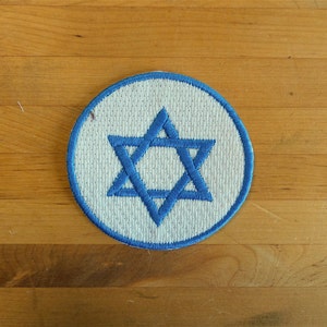 May include: A white circular patch with a blue Star of David embroidered on it.