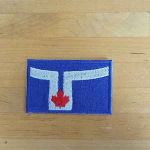 May include: A blue fabric patch with a white stylized letter "T" and a red maple leaf in the center.