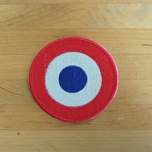May include: A red, white and blue circular patch with a bullseye design. The centre circle is blue, surrounded by a white ring, and then a red ring.