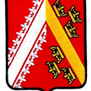 May include: A red patch with a black border, featuring a white and red design on the left and a yellow stripe with six black crowns on the right. The patch has a shield shape.