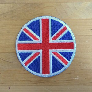 Op de afbeelding: Een ronde geborduurde patch met het ontwerp van de Union Jack-vlag. De vlag is blauw, rood en wit.
