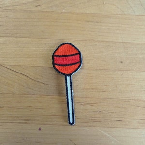 Pode incluir: Uma pirulito vermelha e branca com contorno preto. O pirulito está sobre uma superfície de madeira.