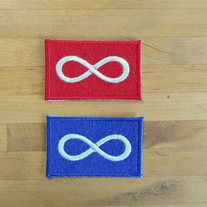 Puede incluir: Dos parches bordados con un símbolo de infinito. El parche de la izquierda es rojo con un símbolo de infinito blanco. El parche de la derecha es azul con un símbolo de infinito blanco.