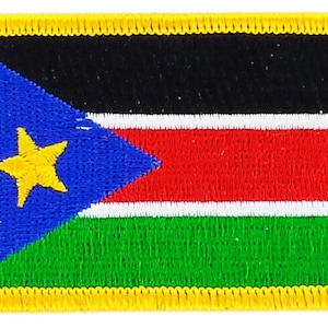 May include: A yellow embroidered patch featuring the flag of South Sudan. The flag design includes a black triangle with a yellow five-pointed star on a blue background, followed by horizontal stripes of red, white, and green.