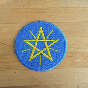 May include: A blue circular patch with a yellow five-pointed star in the center. The star has a sunburst design around it.