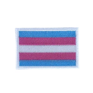 May include: A white embroidered patch featuring the transgender pride flag colours: light blue, pink, white, pink, and light blue.