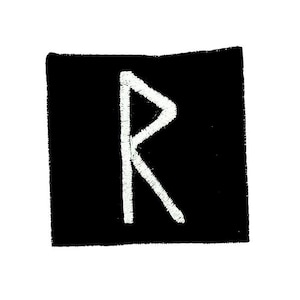 Puede incluir: Un parche cuadrado negro con una letra "R" bordada en blanco. La letra es un diseño estilizado y angular. El parche tiene una apariencia texturizada, lo que sugiere que está hecho de tela.