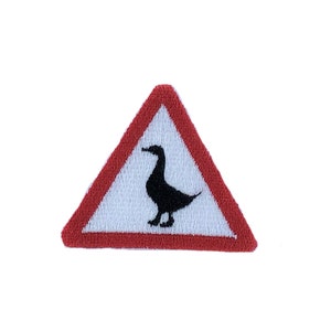 Könnte beinhalten: Ein rotes dreieckiges Warnschild mit weißem Hintergrund und einer schwarzen Silhouette einer Ente darin. Das Schild ist eine Warnung vor Enten, die die Straße überqueren.