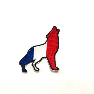 Puede incluir: Parche bordado con la silueta de un lobo aullando. El lobo está coloreado con los colores azul, blanco y rojo de la bandera francesa. El parche tiene un borde negro.