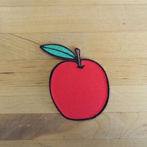 Könnte beinhalten: Ein roter Apfel mit einem grünen Blatt, gestickt auf einem Stoff-Patch.