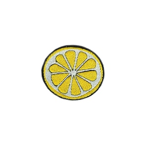 Può includere: Una fetta di limone ricamata, gialla con un centro bianco e un contorno nero.
