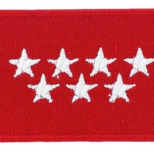 Peut inclure: Écusson rectangulaire rouge avec sept étoiles blanches disposées en deux rangées. Le patch a une bordure cousue, probablement un emblème ou un insigne.