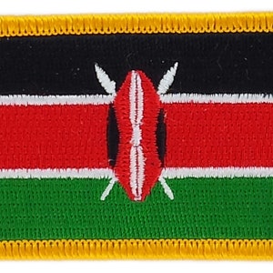 May include: A rectangular embroidered patch featuring the Kenyan flag. The flag is a horizontal tricolour of black, red and green, with a white stripe separating the red and green. A white shield with two spears is centred on the flag. The patch has a gold border.