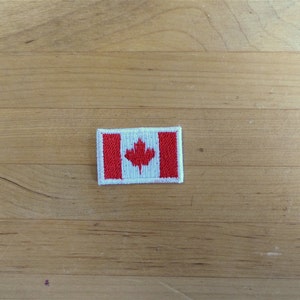 以下が含まれることがあります： カナダの国旗が刺繍された小さなパッチ。旗は赤と白で、中央に赤いカエデの葉があります。
