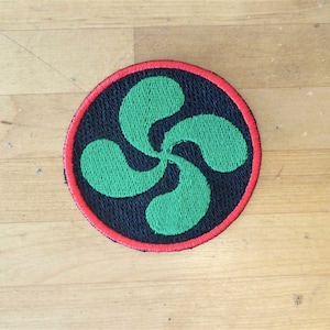 May include: A round, black patch with a red border and a green four-leaf clover design.