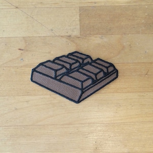 May include: A brown chocolate bar with six squares, outlined in black, on a wooden surface.