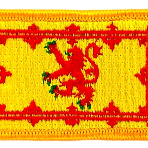 Könnte beinhalten: Ein gelber gestickter Aufnäher mit einem roten Löwen, der auf einem gelben Hintergrund steht. Der Löwe ist von einem roten Rahmen mit dekorativen Details umgeben.