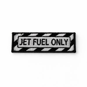Puede incluir: Parche bordado con el texto "JET FUEL ONLY" en blanco, centrado en un rectángulo negro. El borde presenta un diseño a rayas blancas y negras. El parche es rectangular y parece estar hecho de tela.