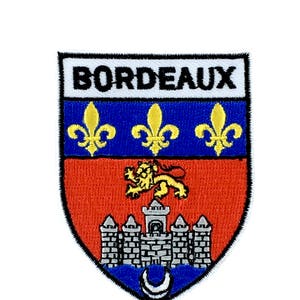 May include: Embroidered patch with the coat of arms of Bordeaux, France. The patch features a red shield with a gold lion, a silver castle, and three gold fleurs-de-lis on a blue background. The text "BORDEAUX" is written in black on a white banner above the shield.